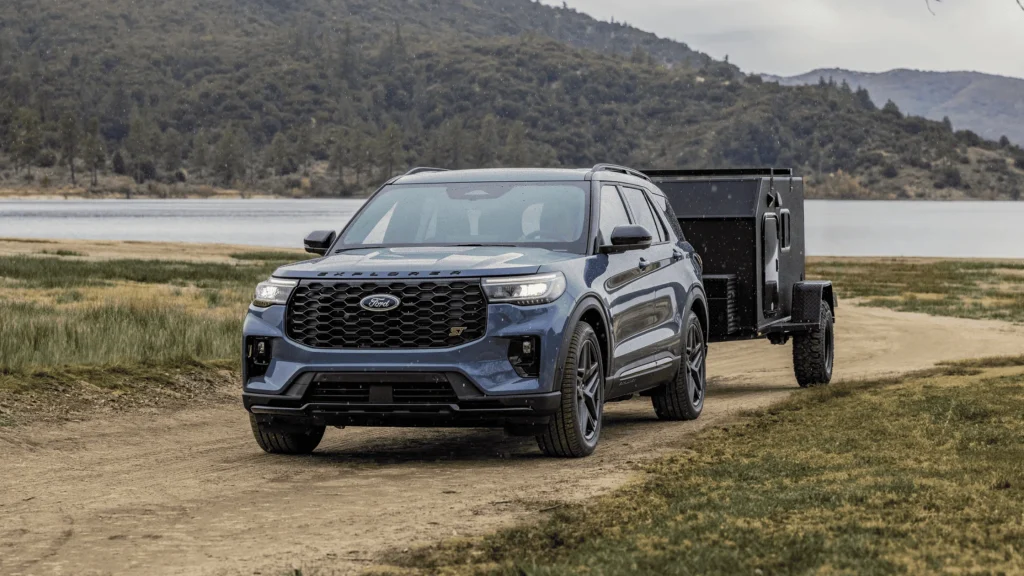 The 2025 Ford Explorer ST towing a camper on a dirt road near a lake, highlighting its impressive towing capacity.