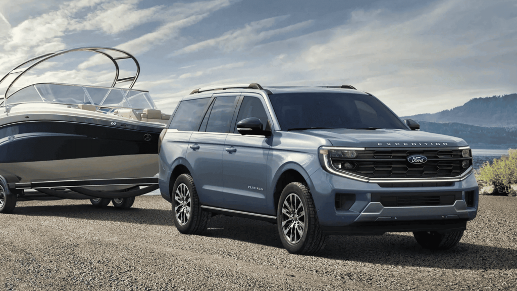 The 2025 Ford Expedition® Platinum in blue towing a luxury boat on a scenic lakeside road. Discover its powerful towing capabilities and premium design for weekend getaways near Cleveland Heights.