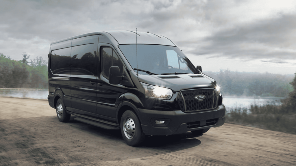 2025 Ford Transit® Van in sleek black, driving on a rural road, built for commercial and delivery efficiency.
