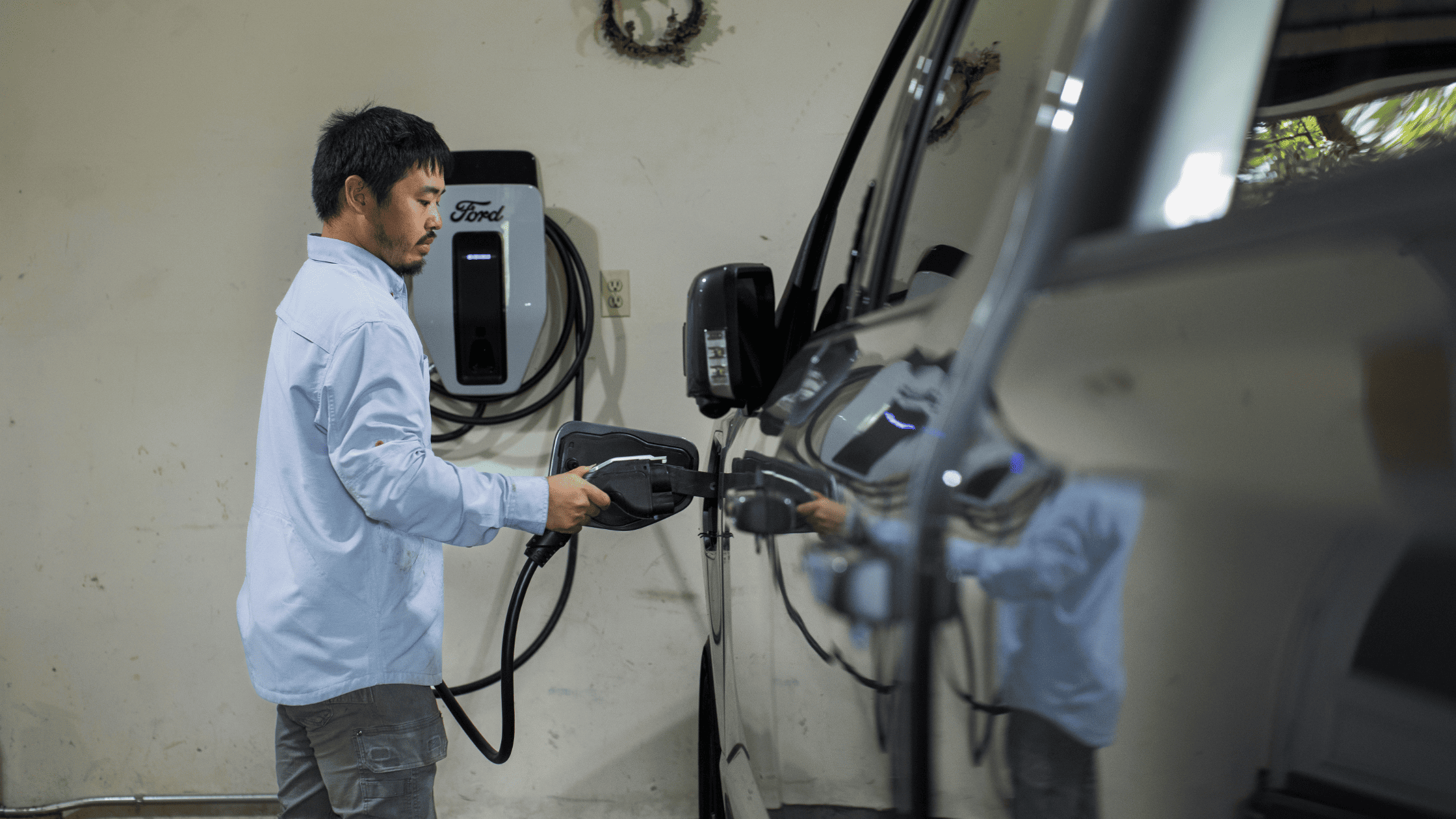 A man plugs in a 2025 Ford F-150® Lightning to a wall-mounted Ford charging station inside a garage, highlighting home EV charging capability.