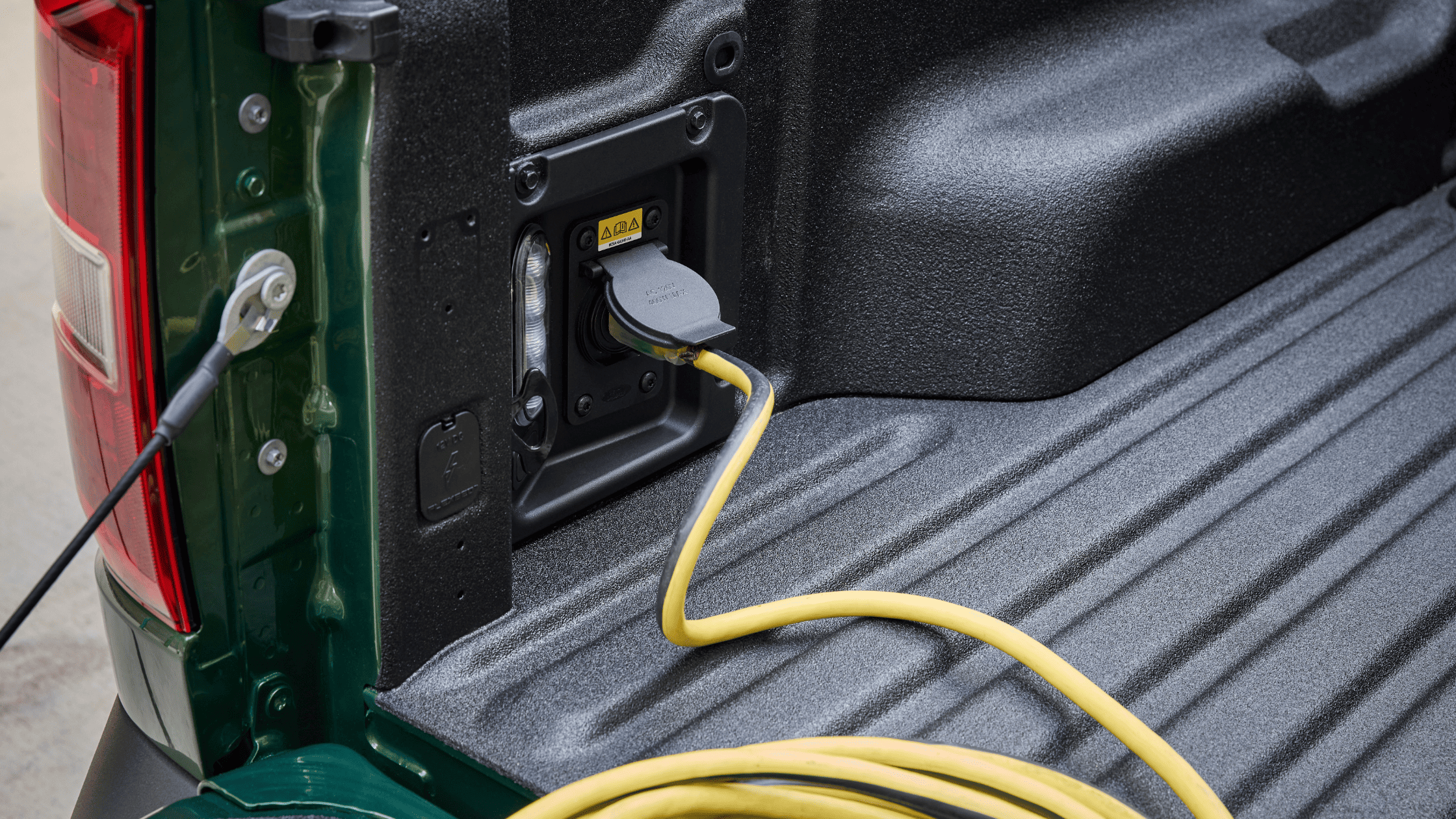 Close-up view of the 2025 Ford Maverick® bed outlet with a yellow cord plugged in, demonstrating its built-in power capabilities for tools and gear.
