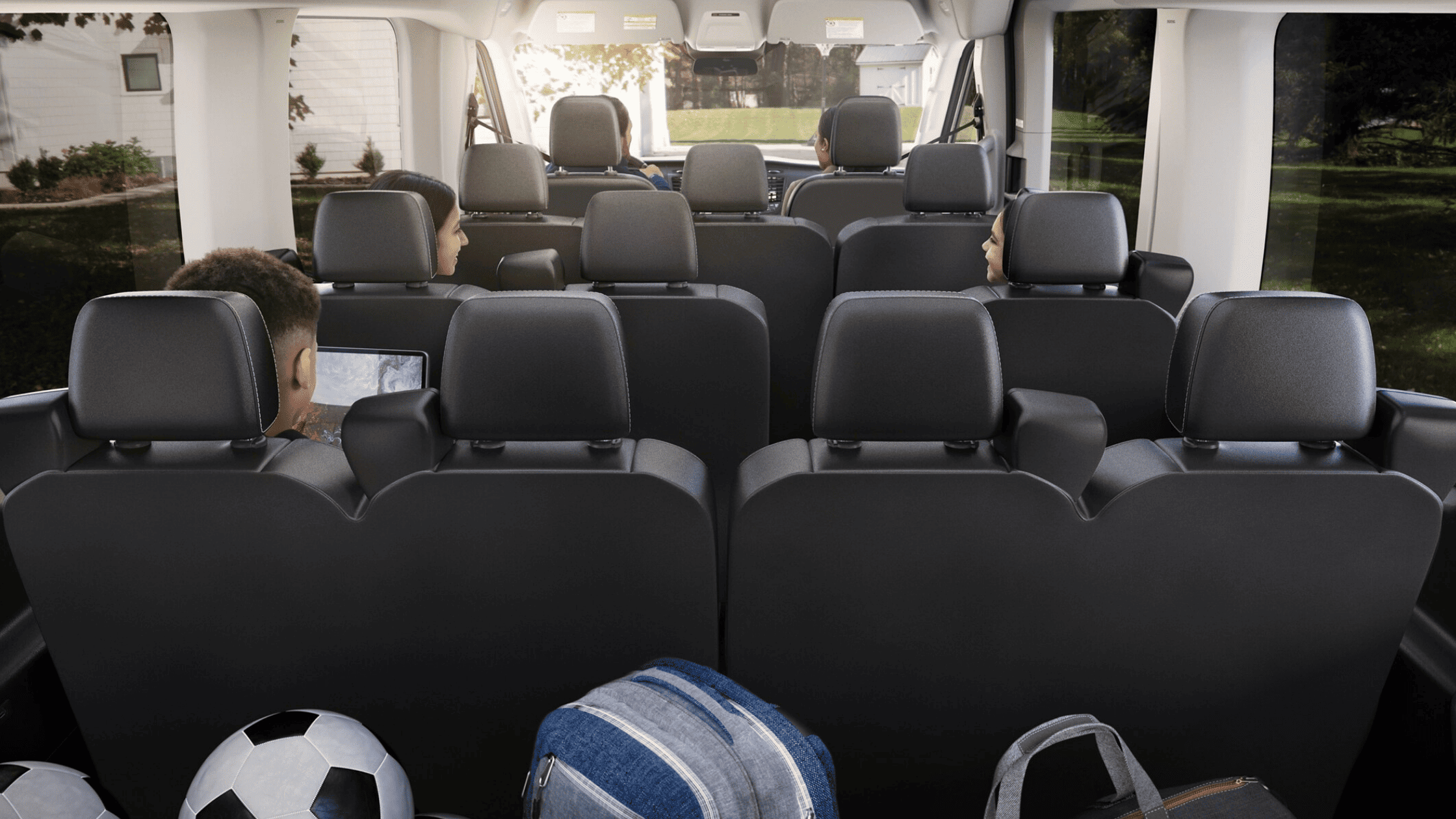 Rear cabin view of the 2025 Ford Transit® showing spacious multi-row seating with passengers onboard and soccer gear in the cargo area.