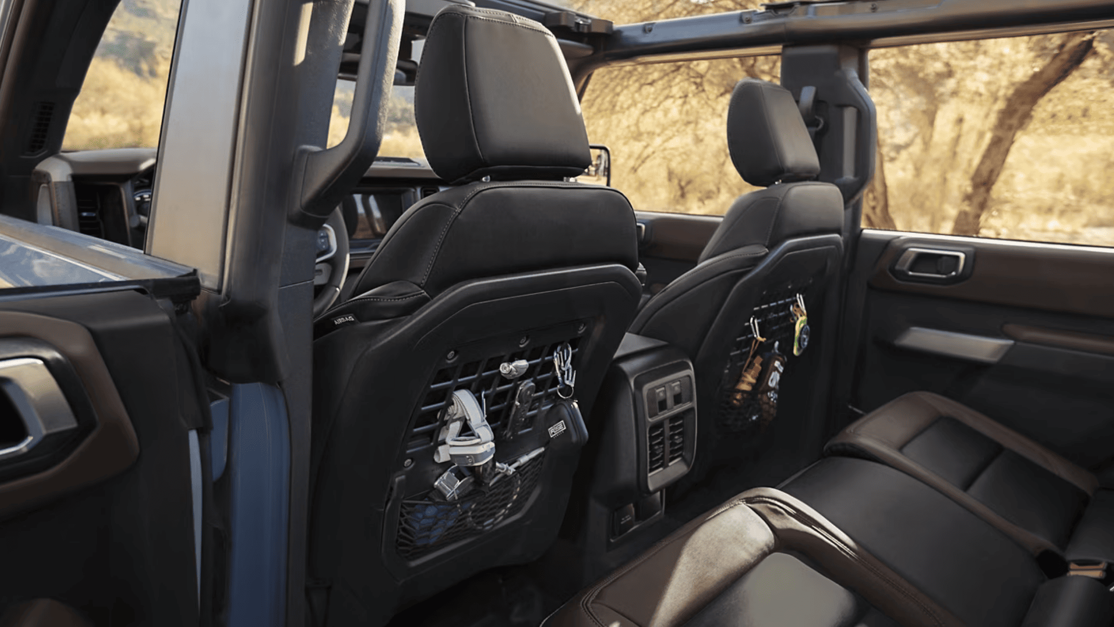 The spacious rear seating area of the 2025 Ford Bronco® with rugged utility features, including seatback storage pockets with off-road gear, under open-air conditions in a desert-like setting.