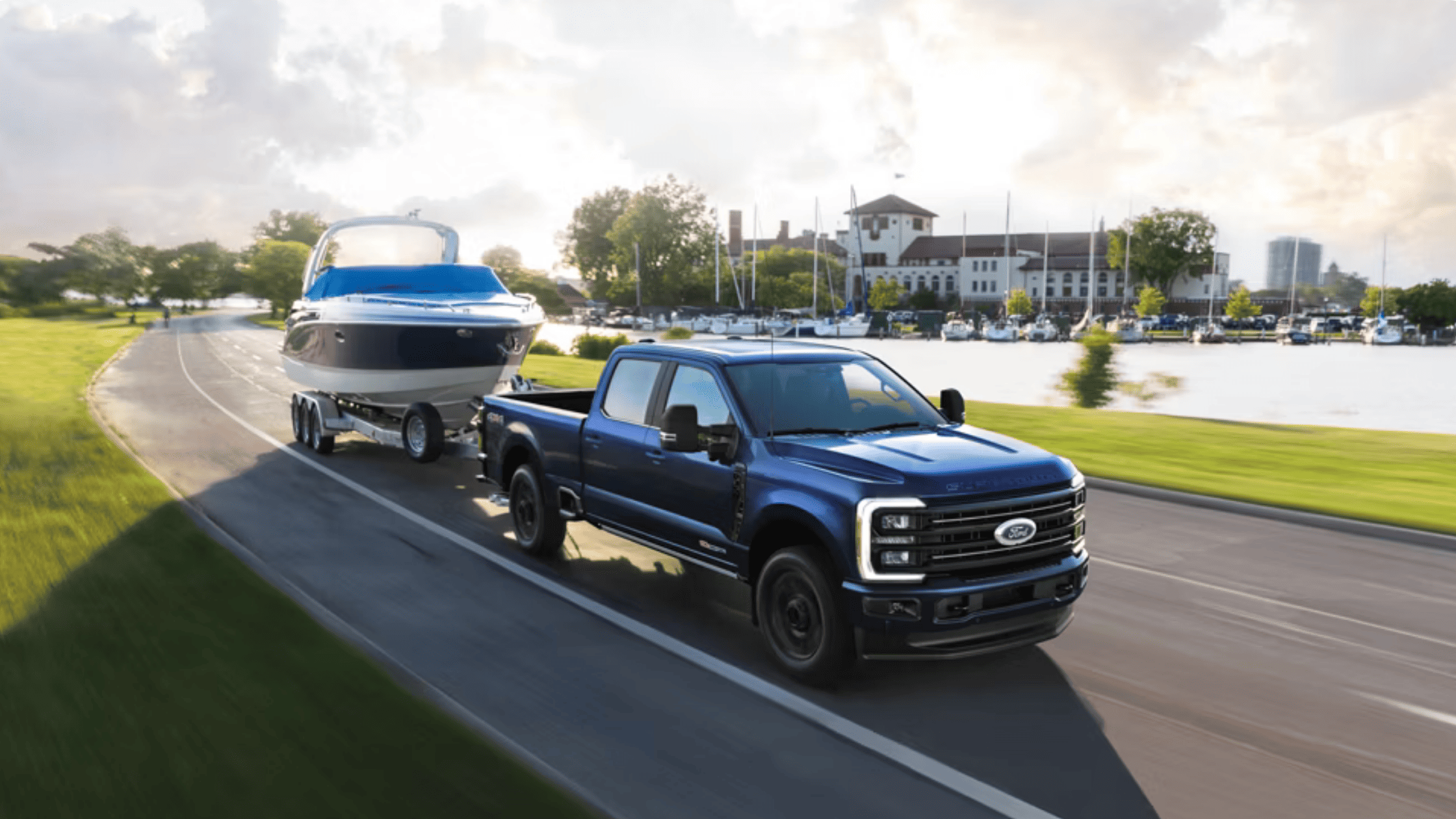 2025 Ford Super Duty® in deep blue towing a large boat along a scenic marina road near Concord, OH.