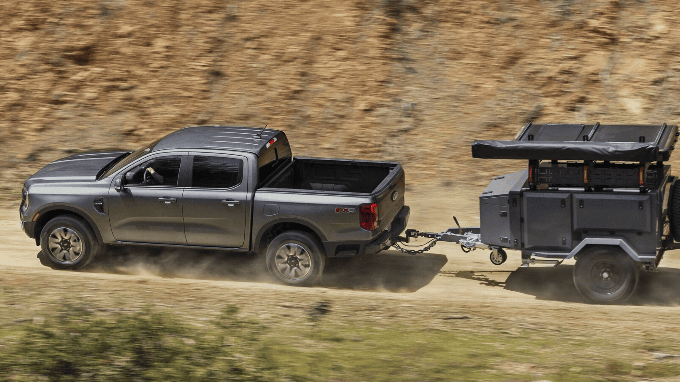 The 2025 Ford Ranger® towing an off-road trailer on a rugged dirt road, showcasing its powerful towing capacity and off-road capabilities.