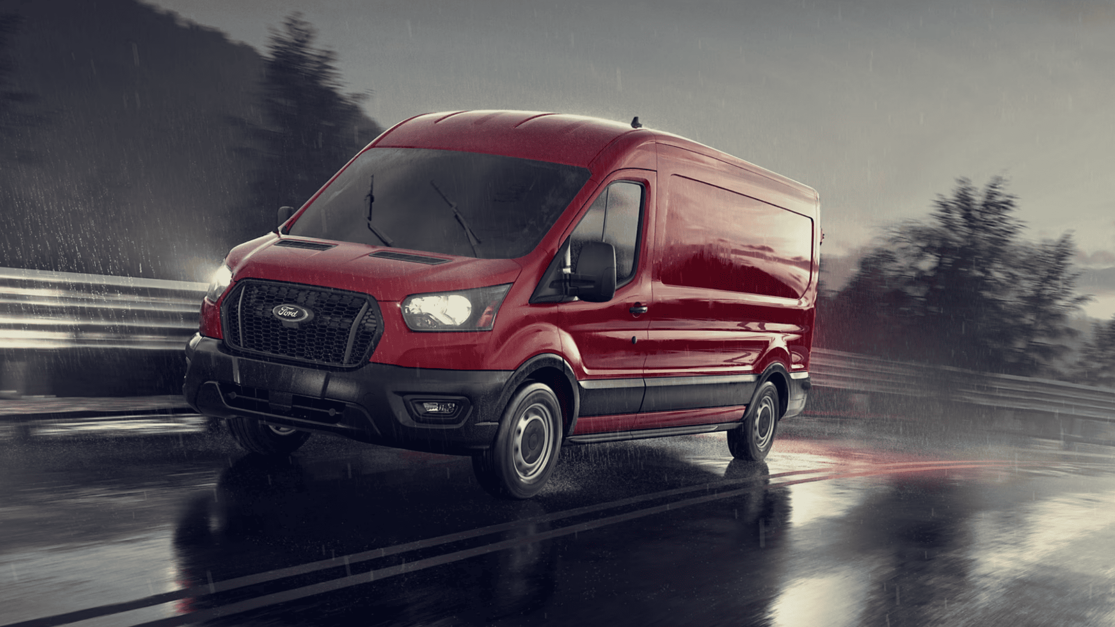 A red 2025 Ford Transit® Van driving on a wet road in the rain, showcasing its capability in challenging weather conditions.